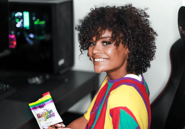 A woman with an afro sits at her work desk holding up a pouch of Unicorn Jerky from Sunday Scaries