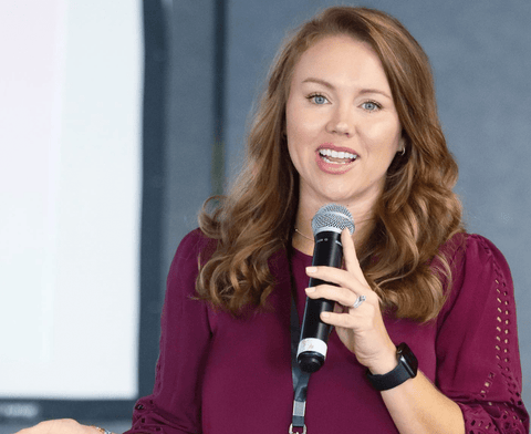 A woman in a maroon shirt with a microphone gives a work presentation