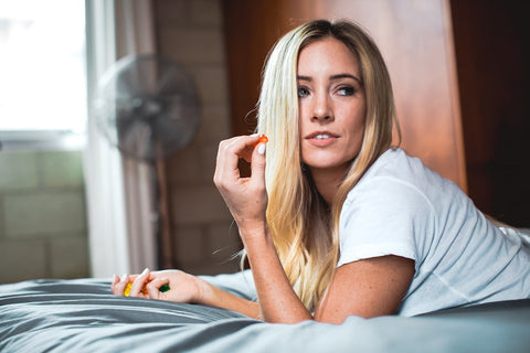 A girl is lying on her bed in isolation holding a CBD gummy