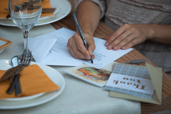 A person writes a handwritten Thank You card at their table