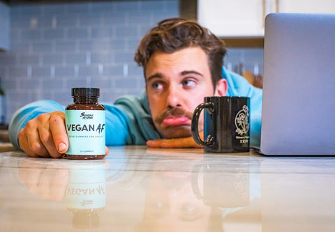 A young professional holds a bottle of Sunday Scaries Vegan AF gummies next to his computer to help with his work stress