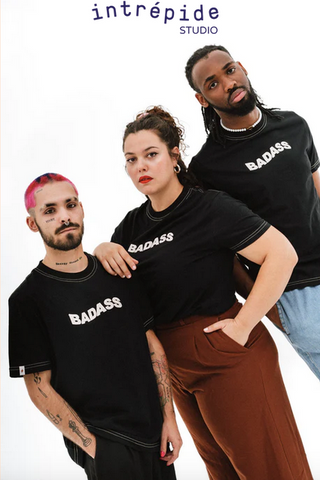 Trois personnes se tiennent debout avec un air sérieux et potentiellement menaçant avec un t-shirt noir sur lequel est inscrit le mot Badass