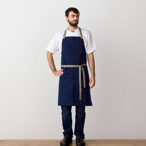 https://cdn.shopify.com/s/files/1/0523/1289/products/chefs-apron-navy-with-tan-straps-men-or-women-textiles-the-reluctant-trading-experiment-2_large.jpg?v=1593297920