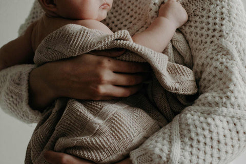 Mutter hält ihr Baby eingewickelt in einer Decke auf dem Arm und kuschelt.