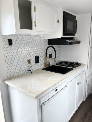 Camper renovation kitchen makeover with herringbone counter, hexagon backsplash, black and gold faucet, and black sink