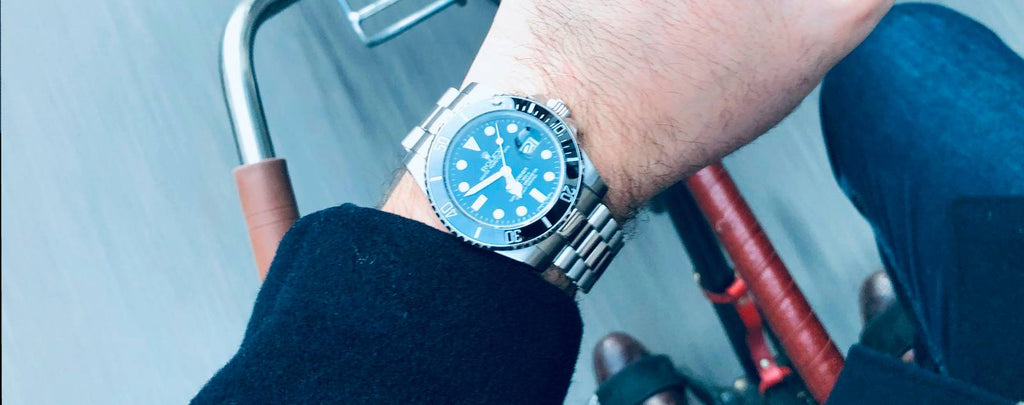 A close-up photo of a person carefully inspecting a Rolex Submariner timepiece with a loupe in one hand and a warranty card in the other hand.