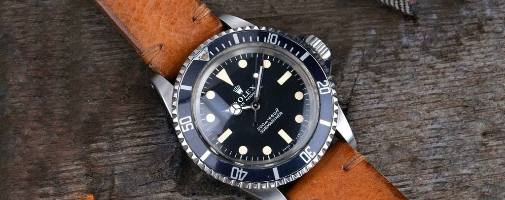 A vintage Rolex Submariner watch with a faded bezel and worn leather strap