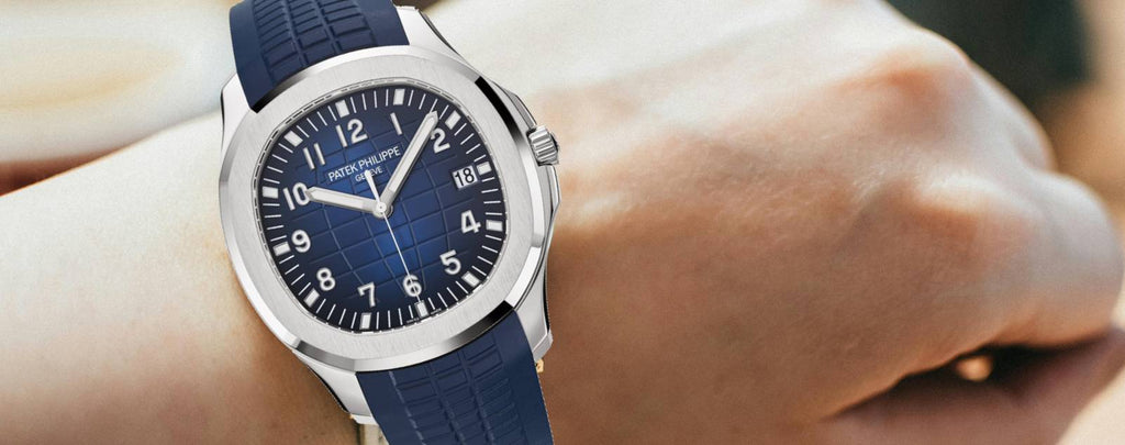 Close-up photo of a Patek Philippe Aquanaut watch on a wrist. Stainless steel case, blue dial with horizontal pattern, blue rubber strap.