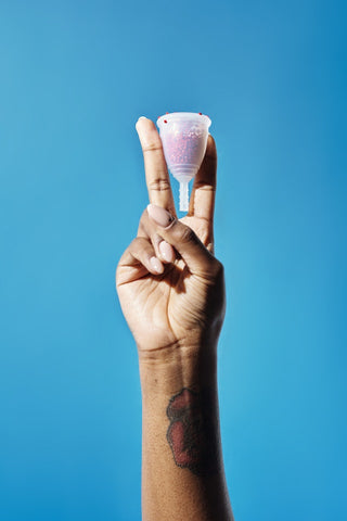 Person doing a peace sign while holding a reusable menstrual cup