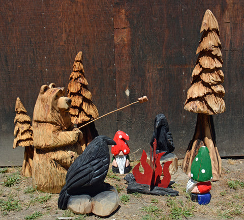 Chainsaw Carving Scene with Bear roasting marshmallow, surrounded by trees, ravens and gnomes. campfire and pole with marshmallows add to these fun scene great display for your garden and yard. business, commercial and residential landscape decorations from California Cedar by Artist and Chainsaw carver Jess Alice