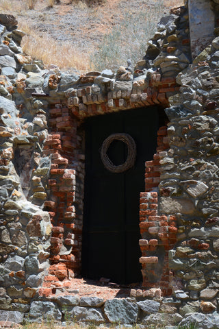 This stunning print of a door surrounded by crumbling brick and grey stone, gives an eerie feeling from the desert of Nevada. Created by Artist Jess Alice titled "Brick Door" This unique piece gives a sense of mystery and wonder about how this door is all that remains. One-of-a-kind wall artwork with neutral colors enhancing any space and  complimenting many aesthetics. Natural reds of brick contrast against cold stone and a dark black door among the sand.   Artwork for residential,  public lounges, cafes, and lobbies. Add interest and conversation starters to your real estate staging, set design, and interior design. Doctor's office, waiting room wall art. Perfect ready-to-hang wall art for guest rooms, beach houses, guest houses, Airbnb, vacation rentals, hotels, motels, and guest suites.