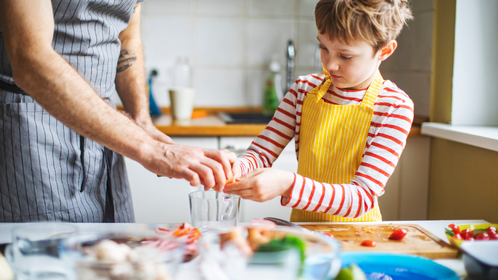 Kid in striped jumper helping his father in the kitchen mixing ingredients in a bowl