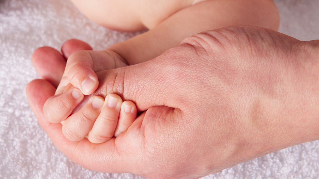 baby's hand with sensitive skin being held by their parent's hand