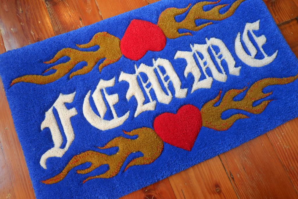 a royal blue hand-tufted queer rug with the word "Femme" on it surrounded by flaming hearts.