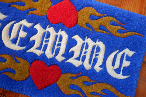 a royal blue hand-tufted queer rug with the word "Femme" on it surrounded by flaming hearts.