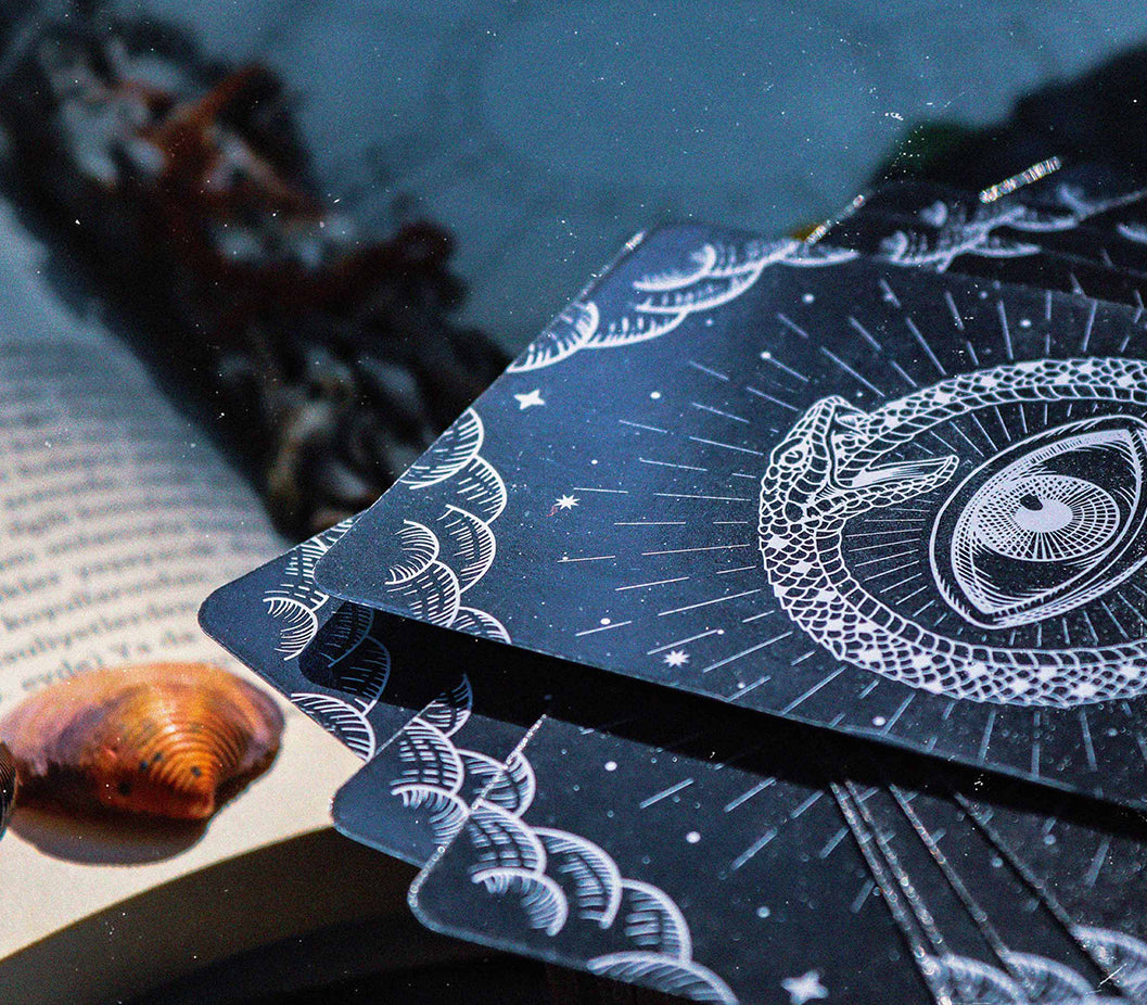 Astrologer and tarot reader Chris Corsini blog post, 10 things you can do to work with this Energy, stack of black tarot cards next to a book and seashell.