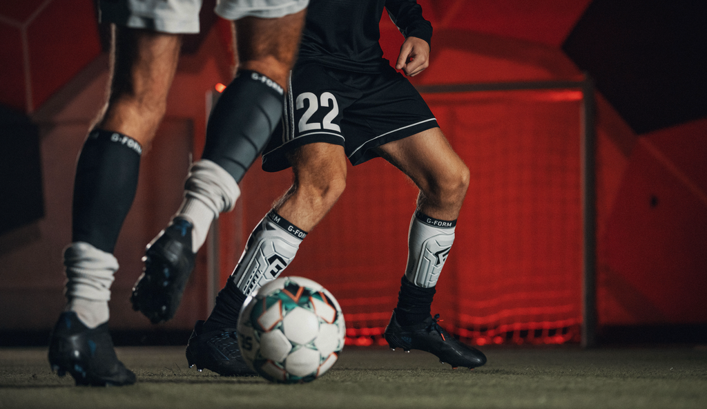 close up of footballers playing with ball wearing black shin guards  