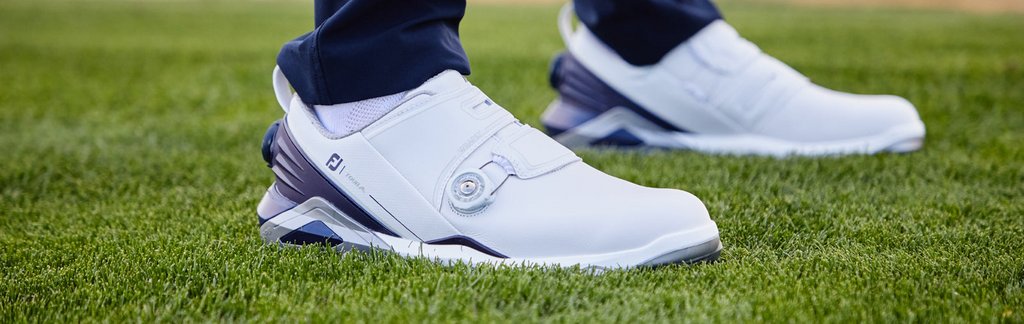 close up of someone standing on green grass wearing footjoy white golf shoes