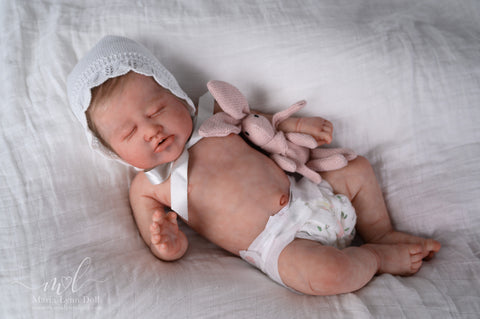 Baby Laurel wearing a white hat and diaper, holding a bunny, and lying on a white blanket