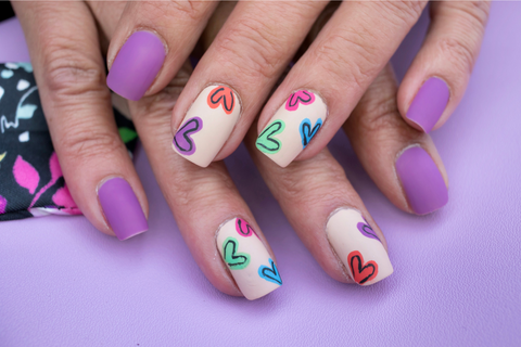 Lavender nails alongside white nails that have coloured hearts on them. These a funky nails for valentine day