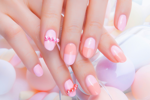 Nail designed to be half and half two colours, one pastel pink and one pastel peach. Two finger nails have tiny pearls lined up on them.