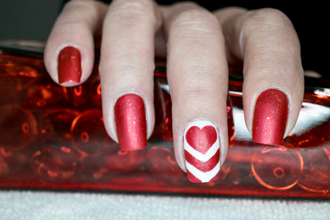 red nails with one accent nail of a light heart and a swirl under it.