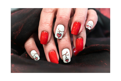 Red nails and white nails. The white nails have drawings of branches on them with hearts dangling down.
