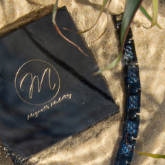 Men's Water Element 4in1 Magnetic Bracelet elegantly placed on sand beside the stylish gift box, with a tranquil water background symbolizing serenity and strength. Perfect for enhancing wellness and personal style.