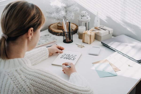 Four tips for sticking to new year resolutions: woman in white sweater writing down her 2022 resolution goals