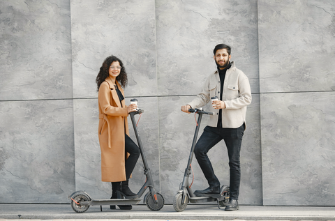 Cheap Transportation Options: A woman and a man stand next to electric scooters and smile at the camera.
