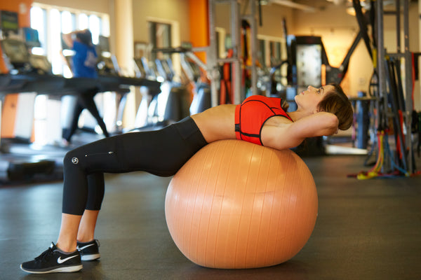 Four tips for sticking to new year resolutions: woman in SportPort red Apex sports bra is working out on a medicine ball