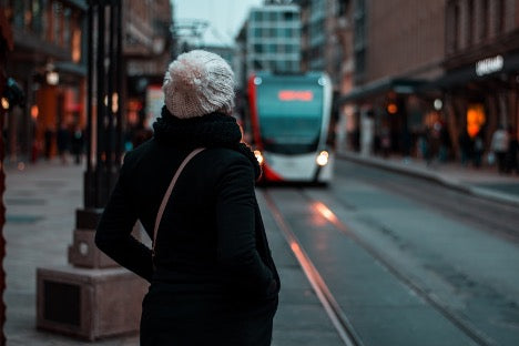 Cheap Transportation Options: A woman looks up the street towards a bus approaching a bus stop.
