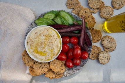 5 Healthy Snacks to Carry On the Go: A plate of fresh vegetables, homemade hummus, and seed crackers is arranged on a stone plate.