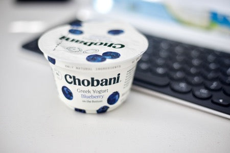 5 Healthy Snacks to Carry On the Go: A blueberry Chobani yogurt sits on a desk in front of a keyboard.