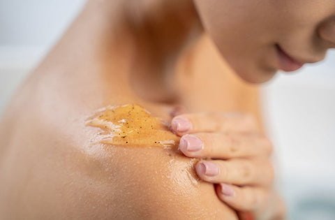 Lady is applying body wash and scrub on her shoulder