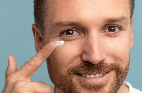 Men is applying eye cream under his eyes