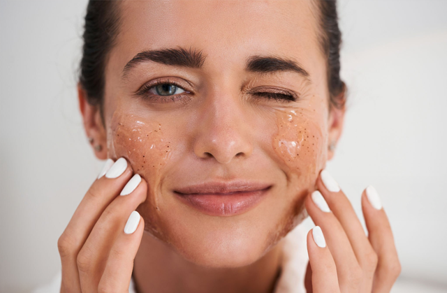 A woman is applying Kumkumadi scrub to her face while playfully winking.
