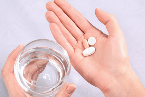 Hands of a  woman holding a glass of water in left hand and 3 pills in her right  palm