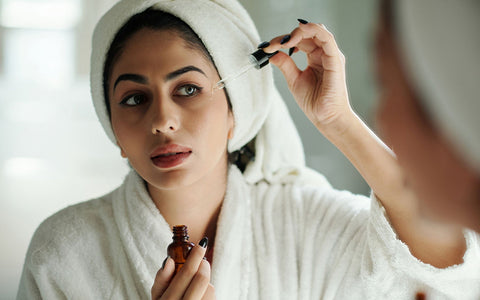 Lady is applying vitamin c serum on her face in front of mirror