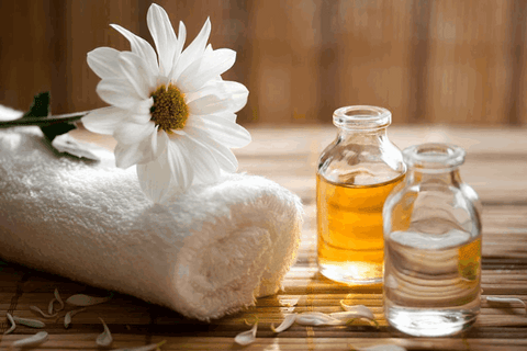 pain relief oil and body oil with white towel and flower are on wooden table