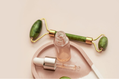 Kumkumadi tailam bottle , applicator and jade roller are on baby pink table 