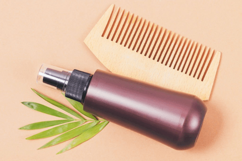 hair serum, comb and leaves are on peach table