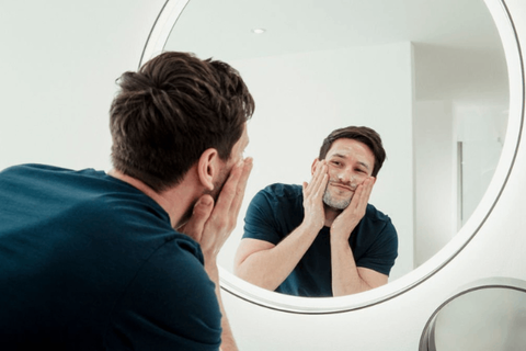 Main is standing infront of mirror and washing his face with ayurvedic face wash 