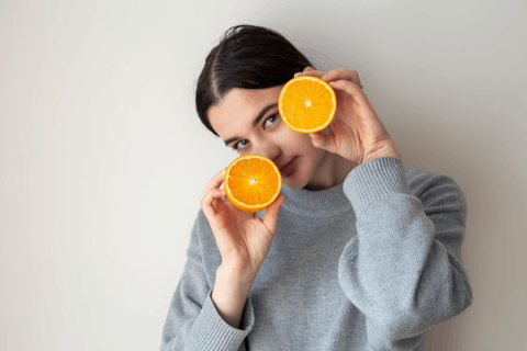 Girl is holding oranges infront of her face 