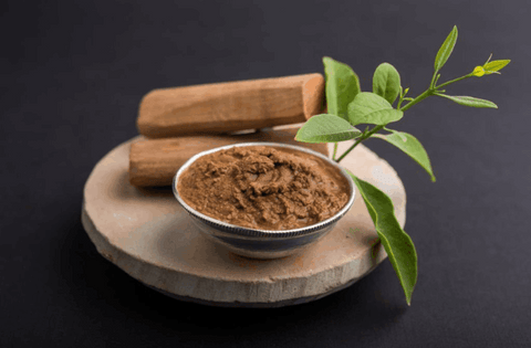 sandalwood powder and with its stick is placed on round wooden coaster with some leaves 