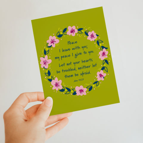 Hand holding a green greeting card with a floral wreath. The words inside the wreath read: Peace I leave with you; my peace I give to you. Let not your hearts be troubled, neither let them be afraid. John 14:27.