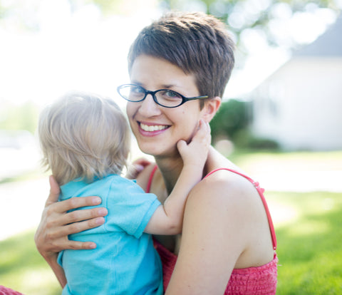 short haired woman smiling at camera, holding small child whose face is turned away