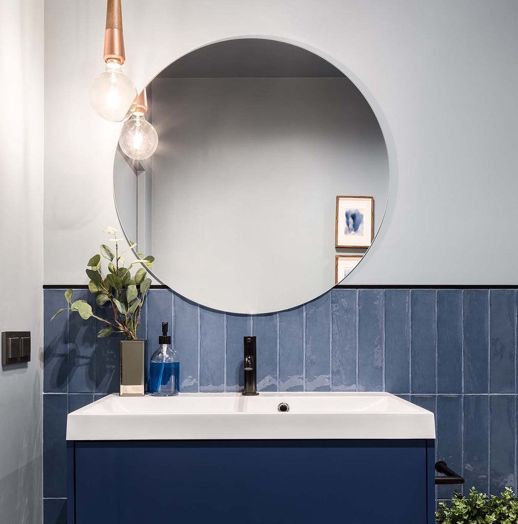 blue vanity with large round frameless mirror and vintage lighting 
