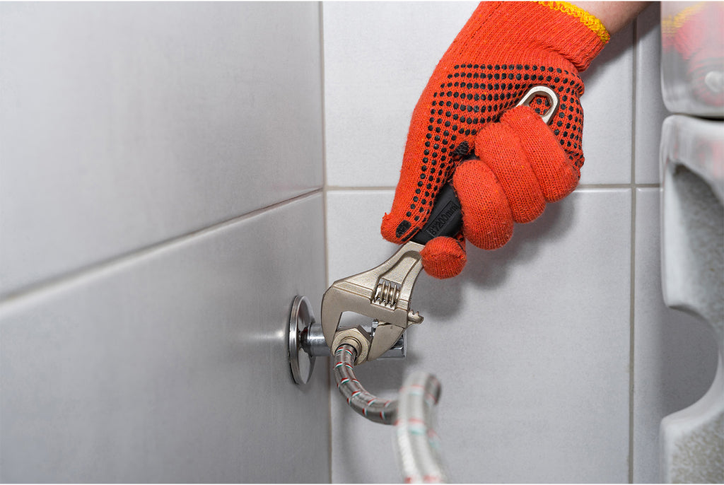 Plumber installing a water hose for the toilet with orange work gloves
