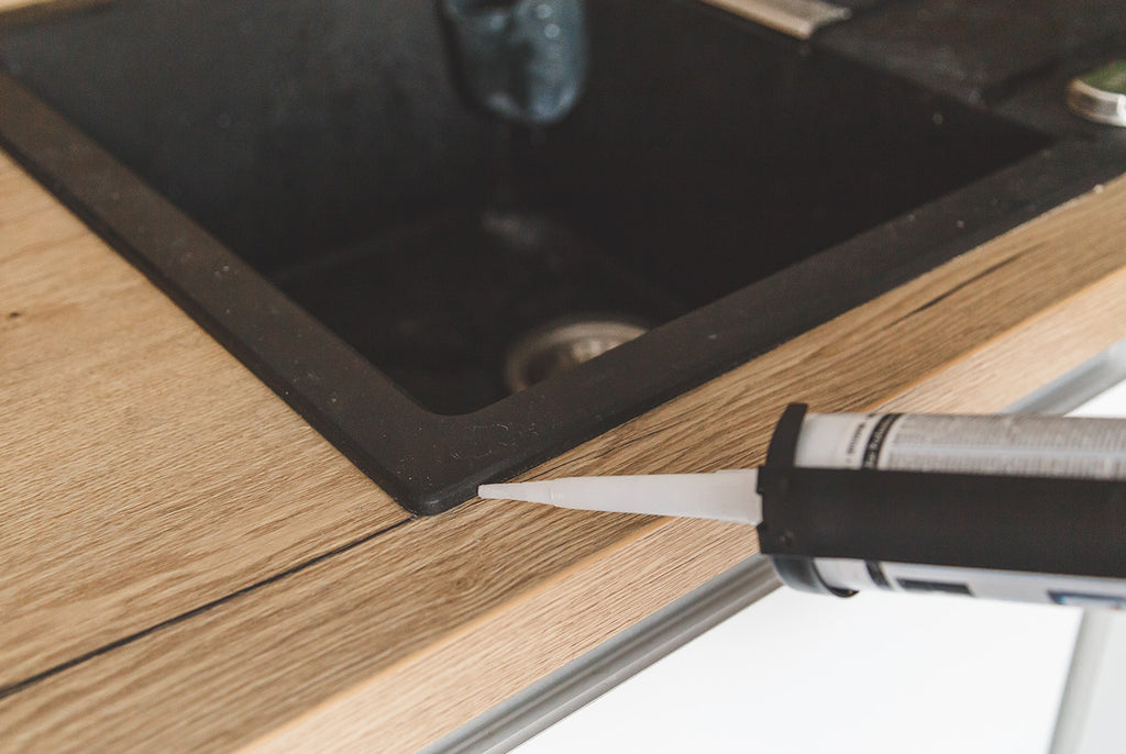 caulking the corner of a black dropin sink on a woode ncountertop